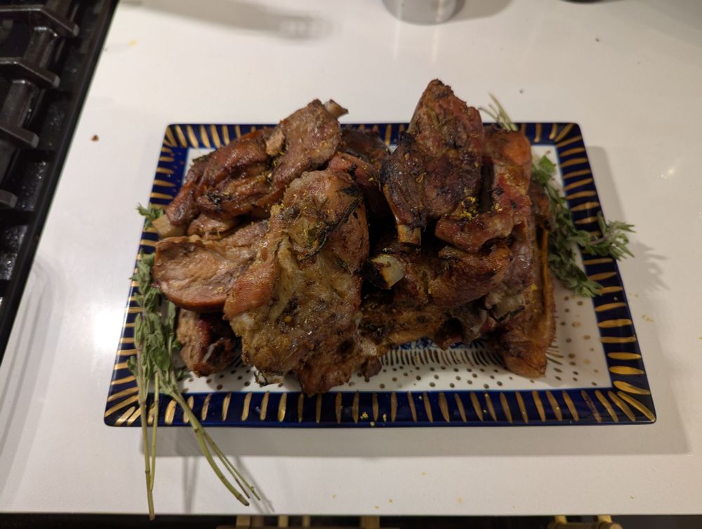 A platter of browned ribs with spices and a bit of lemon zest, garnished with fresh oregano.
