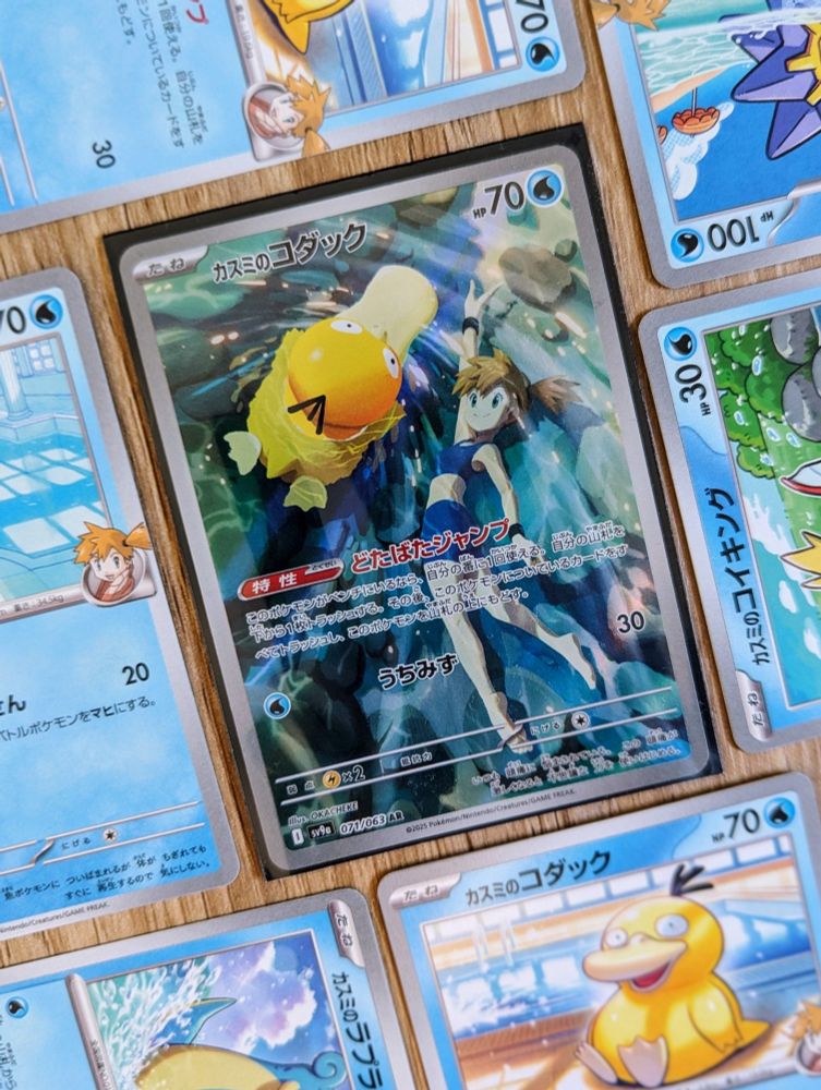 Flat lay photo of a Japanese art rare Pokemon card. Featuring Misty swimming underwater in a clear river with Psyduck swimming on the surface. Surrounded by other common misty's Pokemon cards. 