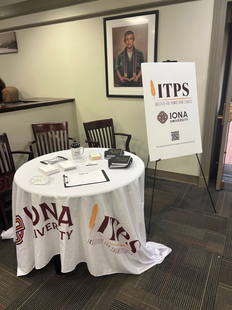 A white table with brown chairs with a clipboard and planners next to a poster on an easel with the ITPS burgundy and gold logo