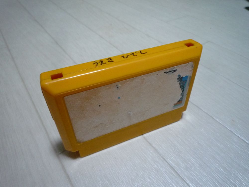 オレンジ色のファミコンのカセット。上の面にマジックで「うえき ひでし」(?)と書かれている。ラベルがほとんど剥がれてしまって一見なんのゲームかわからない...