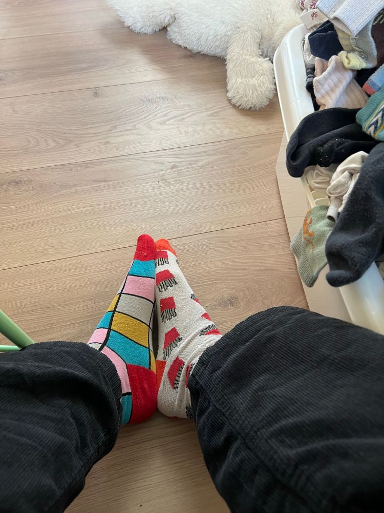 Ein Bild von meinen Füßen neben einem Wäschekorb. Ich habe unterschiedliche Socken an.