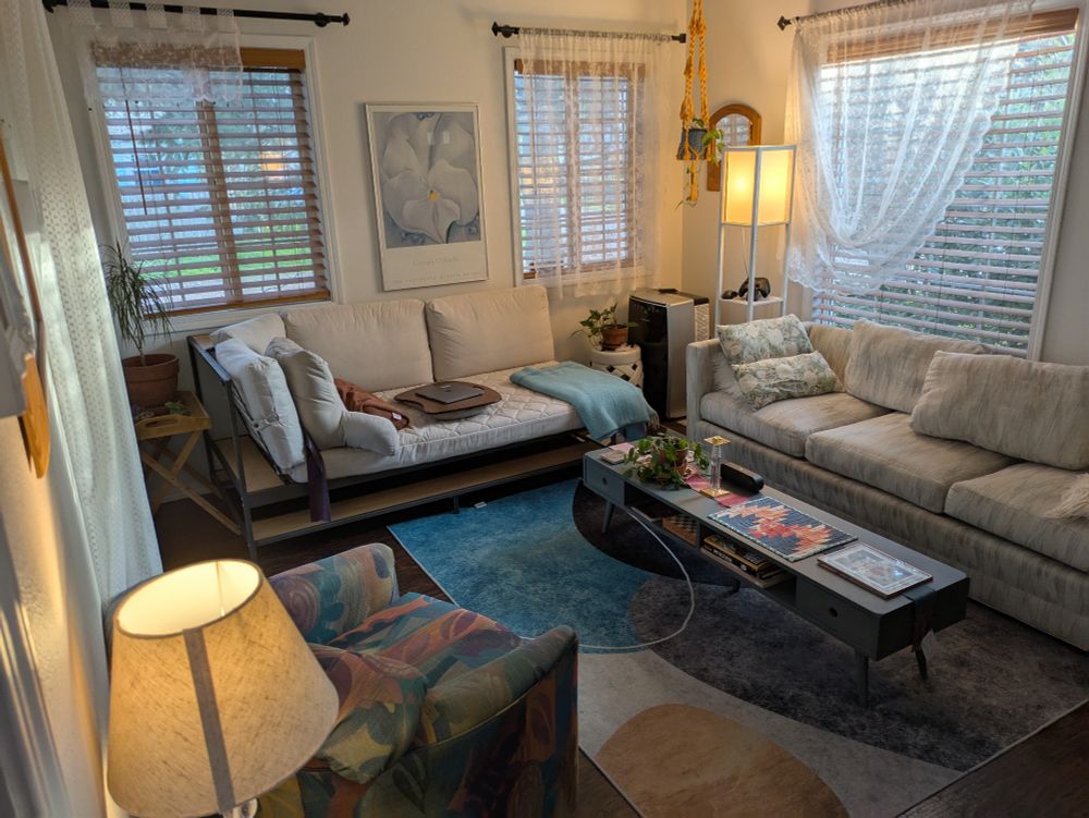 photo of a living room with white curtains, wooden shades, and pastel colors all over. 
