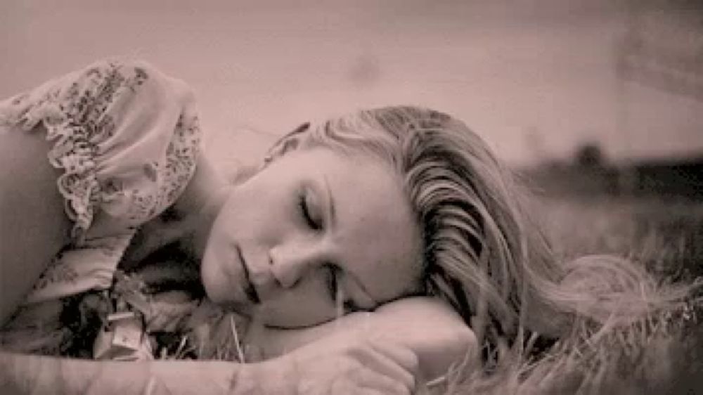 a woman is laying in the grass with her eyes closed and her head on her arms .