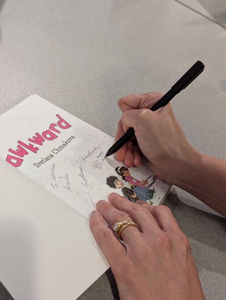 A photo of Svetlana Chmakova signing a copy of Awkward