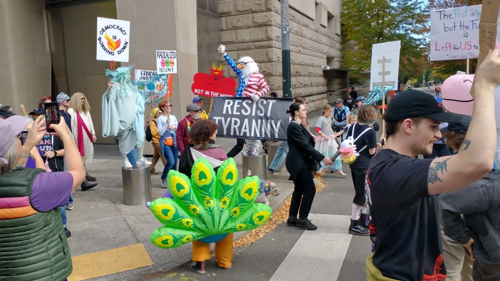 More people at the protest, most notably a woman dressed as the Statue of Liberty (with a sign saying "Democracy is Burning Down") and someone dressed as a bald eagle in an American flag suit (with a sign saying "Resist Tyranny").