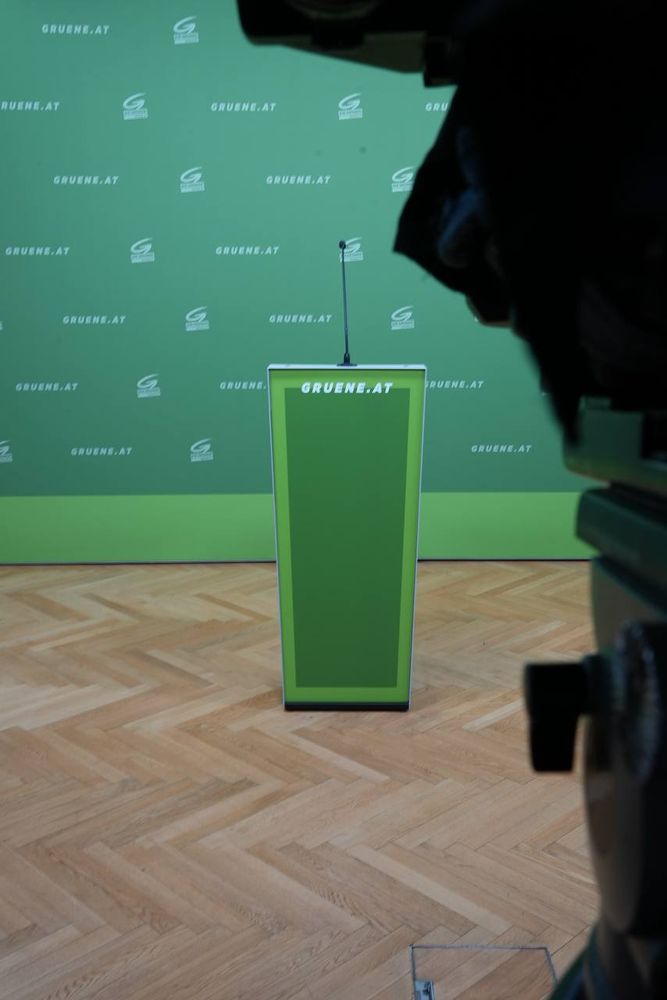 Redner:innenpult im Grünen PK-Raum, vor grünem Backdrop, auf dem gruene.at steht