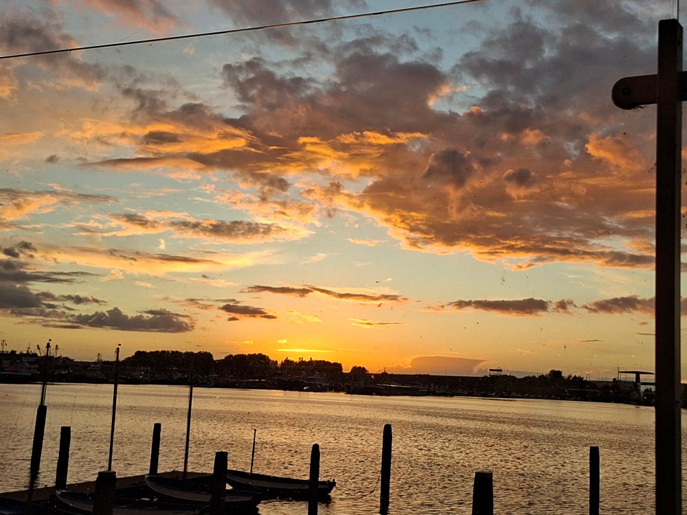 Sonnenuntergang über dem Meer. Es isg scjon relativ dunkel, die Sonne färbt alles intensiv gelb-Orange. Links unten sieht man  die Umrisse von kleinen booten. Im Horizont.wwirere Umrisse größerer schoffe