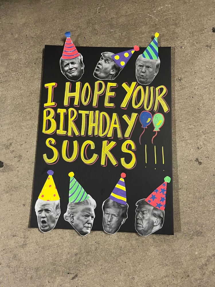 A protest sign that says “I hope your birthday sucks!” With photos of Donald trump in party hats