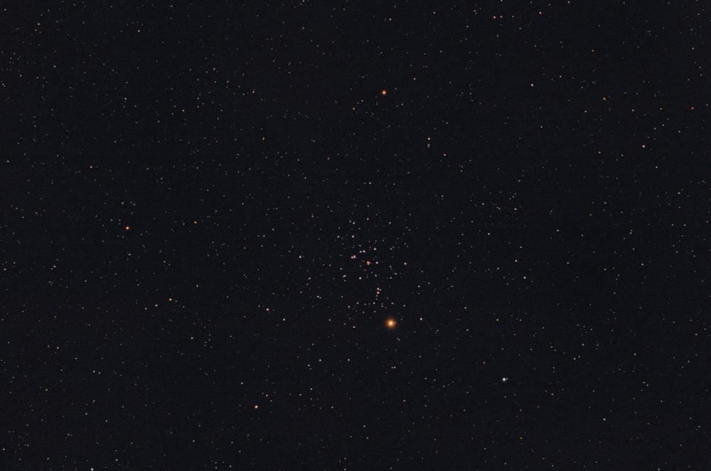 A field of stars, with an open cluster (M44, the Beehive Cluster, or Praesepe) near the middle. Right below the cluster, the planet Mars, visible as a bright orange-red star.