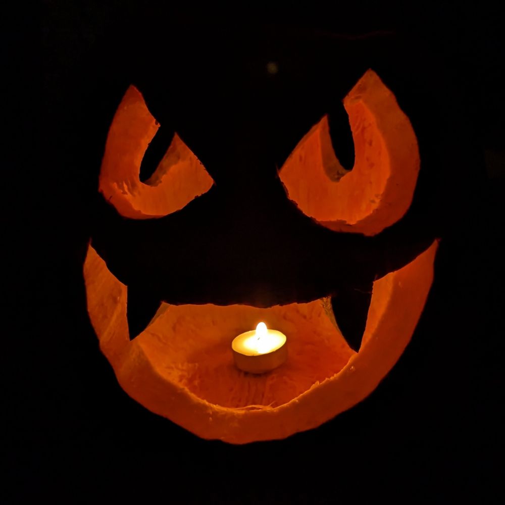 A pumpkin carved to resemble Gastly's face lit by a lil candle.