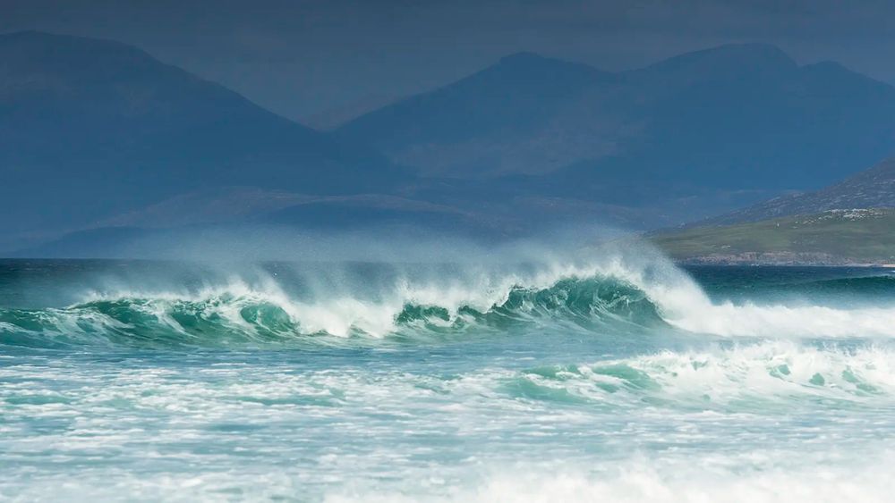 White horse waves rolling in at the beach, with mountains in the background