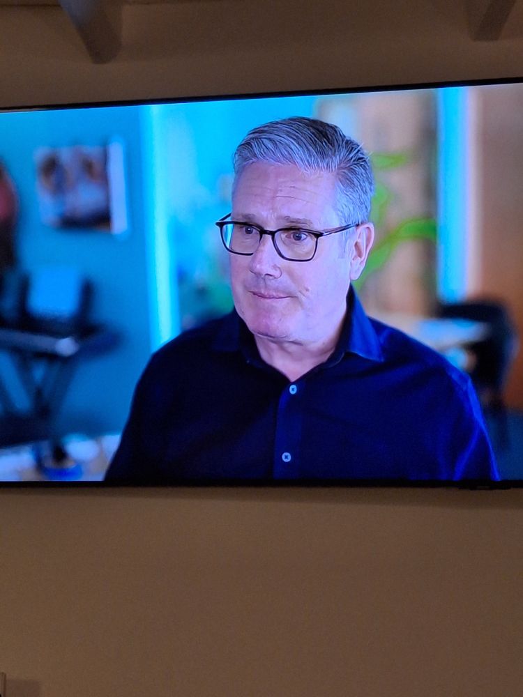 Keir Starmer on TV wearing a fashionable dark blue shirt and glasses.