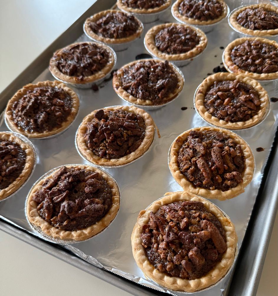 Fifteen three-inch chocolate pecan pies on a baking sheet.
