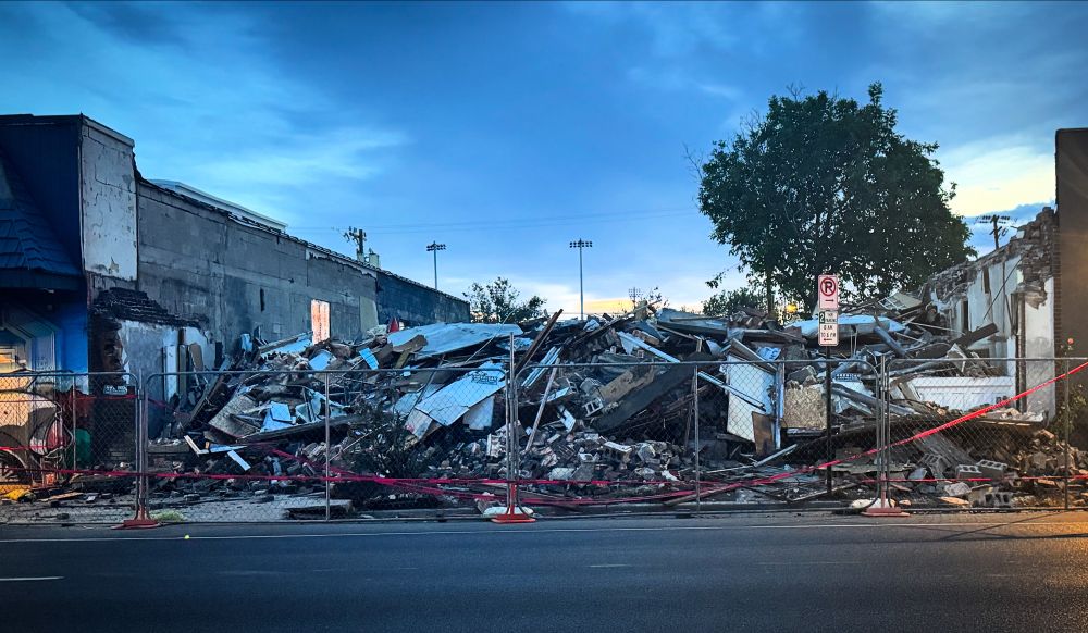 A photo of a pile of rubble between two buildings on a wide street. Photo taken at dusk.