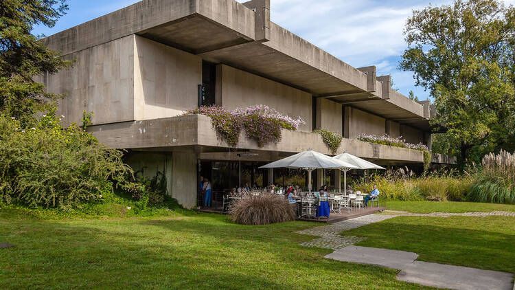 Exterior: concrete, angled, square. Low profile. Umbrellas with tables suggest the outdoor seating of a cafe. 