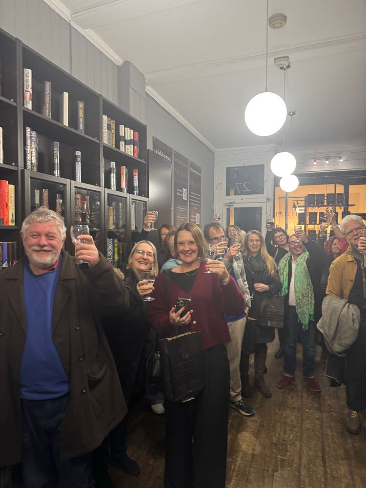 Crowd of cheery, cheersing people holding up their glasses at the book launch in book shop 