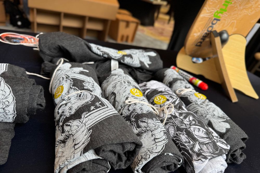 Stack of Honeybadger branded t-shirts featuring detailed black and white illustrated designs with badger artwork, displayed on a conference table with yellow circular stickers that read "XS."