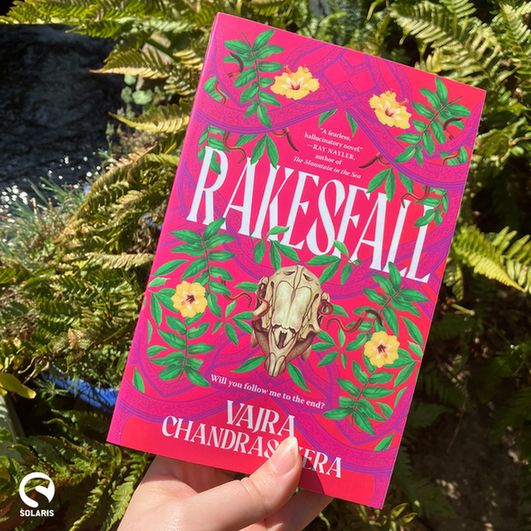 A copy of Vajra Chandrasekera's RAKESFALL held up against some green ferns.

The white Solaris logo is in the bottom left corner.