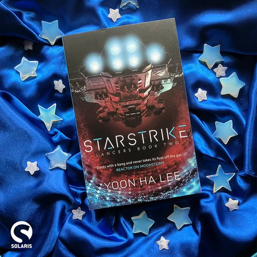 Against a blue fabric background dotted with stars, a flatlaid copy of STARSTRIKE by Yoon Ha Lee. The white Solaris logo is in the bottom left corner.