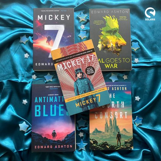  Against a background of teal fabric divided into four quadrants by crystal stars, four flatlaid paperbacks by Edward Ashton: MICKEY7, ANTIMATTER BLUES, MAL GOES TO WAR and THE FOURTH CONSORT. The movie tie-in edition of MICKEY7 is laid on top. The white Solaris logo is in the bottom left corner.