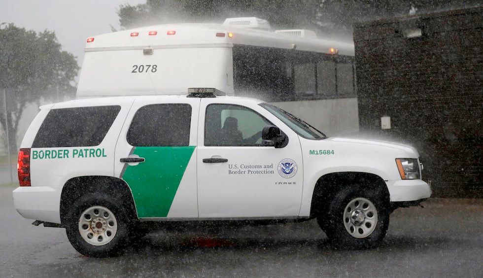An image of a Border Patrol vehicle in the rain. The vehicle is a white SUV with police lights on top, tinted windows, and a large, diagonal, green stripe towards the back seat doors. There is also green writing on the side that says "Border Patrol" and smaller writing on the side door that says "U.S. Customs and Border Protection" and then the seal of the US Homeland Security department