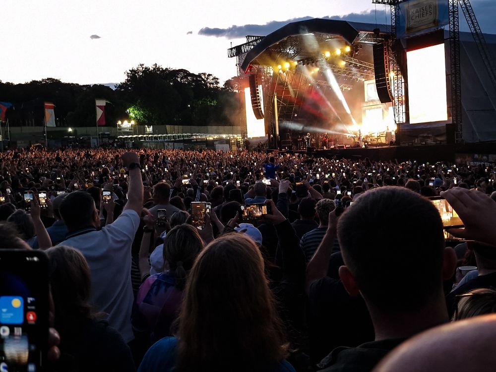 A large crowd at an outdoor stage. Almost all taking videos on their phones.