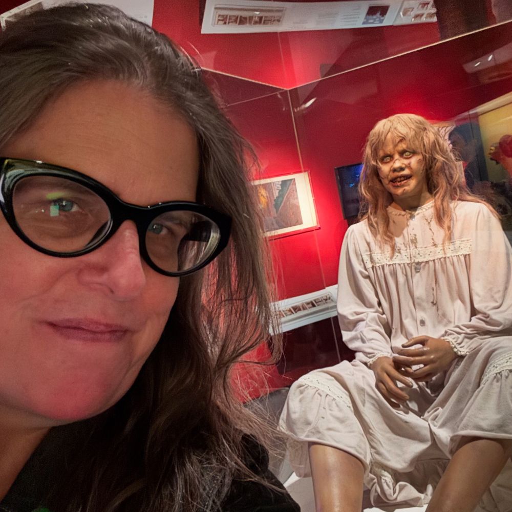 A woman wearing glasses posing next to a model of Linda Blair in The Exorcist