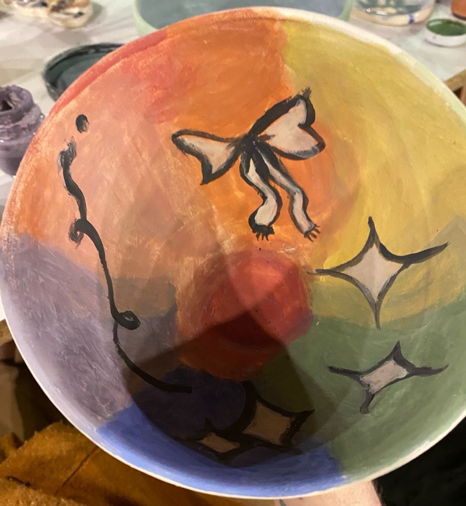 The bowl inside is rainbow themed and has multiple stars, one big ribbon and a dark lace all drawings on top of the rainbow.