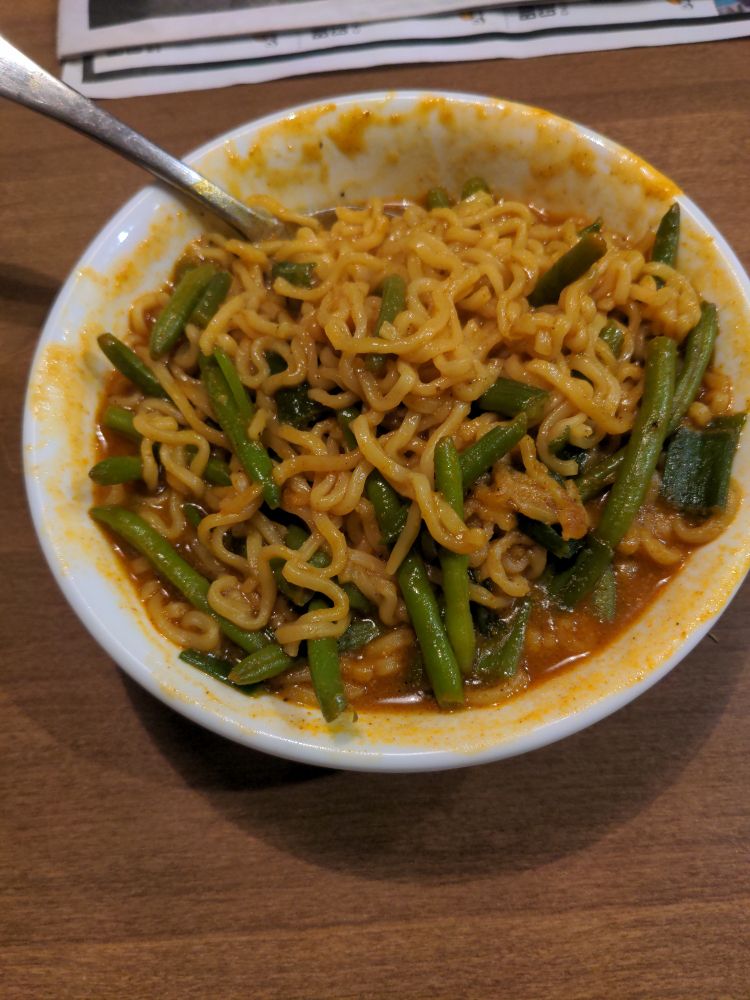 A bowl of ramen noodles in a spicy yellow curry sauce with sliced green onion tops and green beans