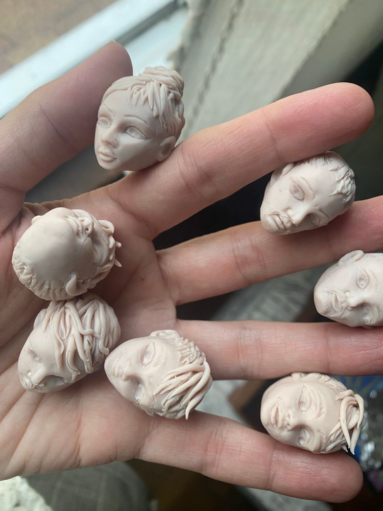 Brandy’s hand with multiple small clay heads fashioned and sculpted and oven dried 