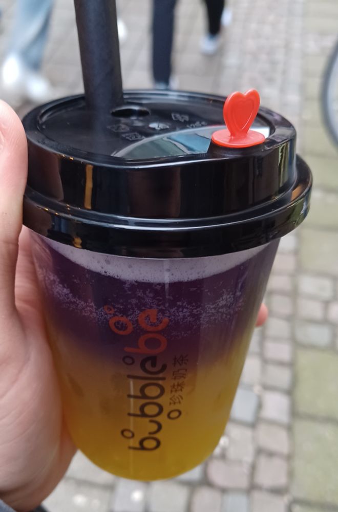 Foto: Ich halte einen Becher Bubble Tea. Die obere Hälfte ist lila, die untere gelb.