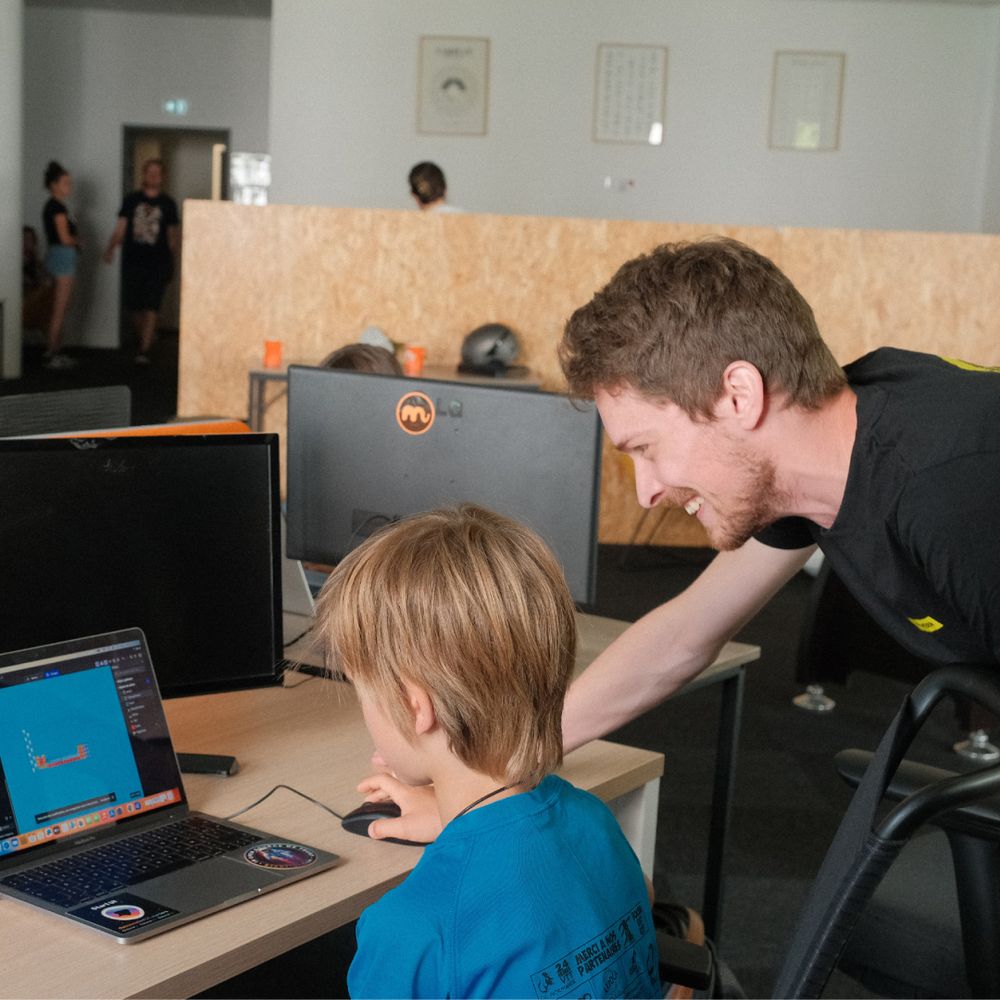 Renan aide un enfant pout l'exercice de son atelier "Créer mon mini jeu-vidéo"