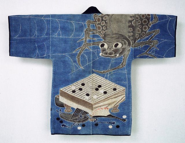 official museum photo of the object on white background: "A large spider-with an endearing face-looms over the shoulder of the jacket, where it hovers menacingly over an abandoned go board. The range of tonalities centers on indigo, white, black, and greyish-brown, with red accents on the fan; this color palette visually unites the work, creating parallels between the spider's eyes and the go pieces." 

“The oversized spider hovering over the go board alludes to Tsuchigumo ("Earth Spider"), the Noh drama that tells the story of the warrior Minamoto Yorimitsu fighting off the monstrous earth spider, who is disguised as a monk.”

“The jacket tells a story from the life of Minamoto no Yorimitsu (948–1021), a warrior-hero. The story is as follows: Yorimitsu was sick, and was resting in bed. He was visited by a priest—but the priest was actually a giant spider (tsuchigumo) in disguise! Yorimitsu, being very clever, sees through the disguise, and attacks the spider with his sword, wounding him. Yorimitsu’s four attendants, called the Four Heavenly Kings, were playing a game of go while guarding him, and leapt up to track the spider back to his den.[2]

This narrative was popular in theatrical productions, and there was a song in Noh theatre specifically about tsuchigumo, the intimidating earth spider. The story appears frequently in woodblock prints in the nineteenth century as well. The jacket shows the moment when the go game was abandoned, with tsuchigumo retreating back to his web. So great was the hurried effort to find the spider that the attendants left behind their personal effects, scattering go pieces in their haste.”