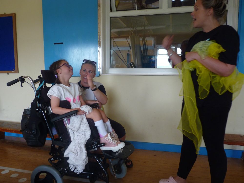 A girl in a wheelchair smiles at a dance teacher 