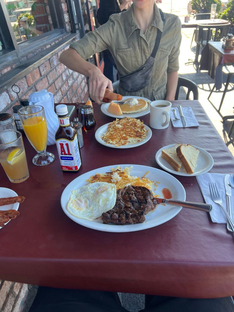breakfast of steak & eggs with a side of bacon and a short stack of pancakes