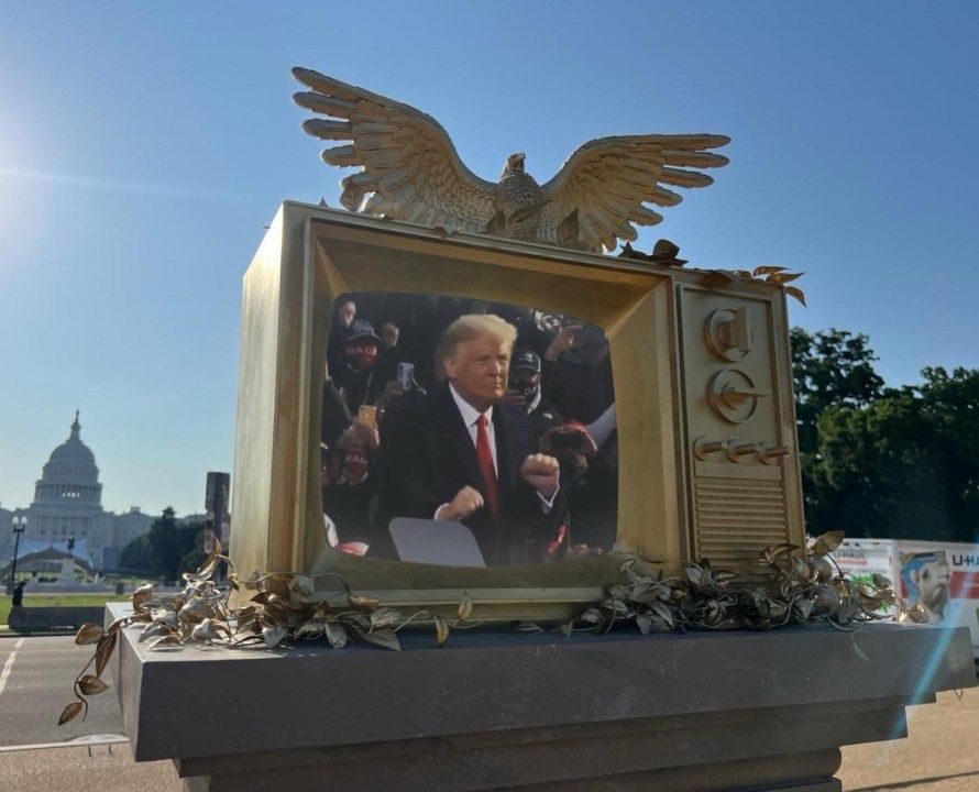 An art installation featuring a giant gold tv with an eagle on top and an image of Trump dancing. 