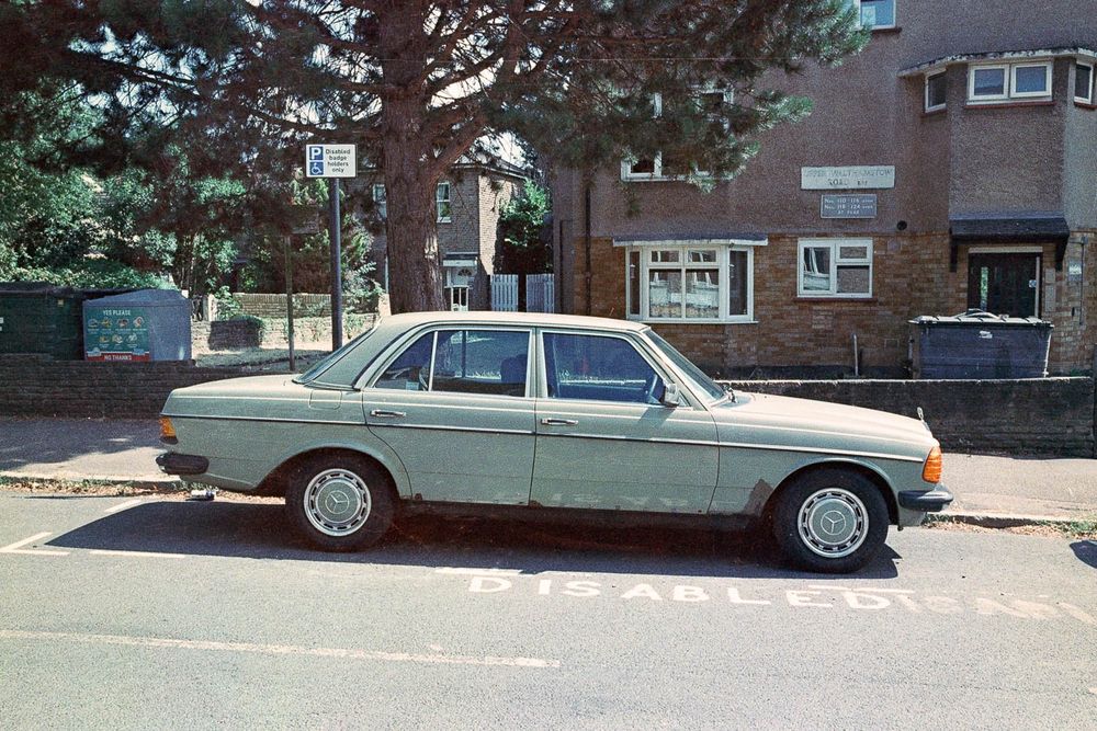 A battered old Mercedes parked in a disabled bay in front of a block of flats.