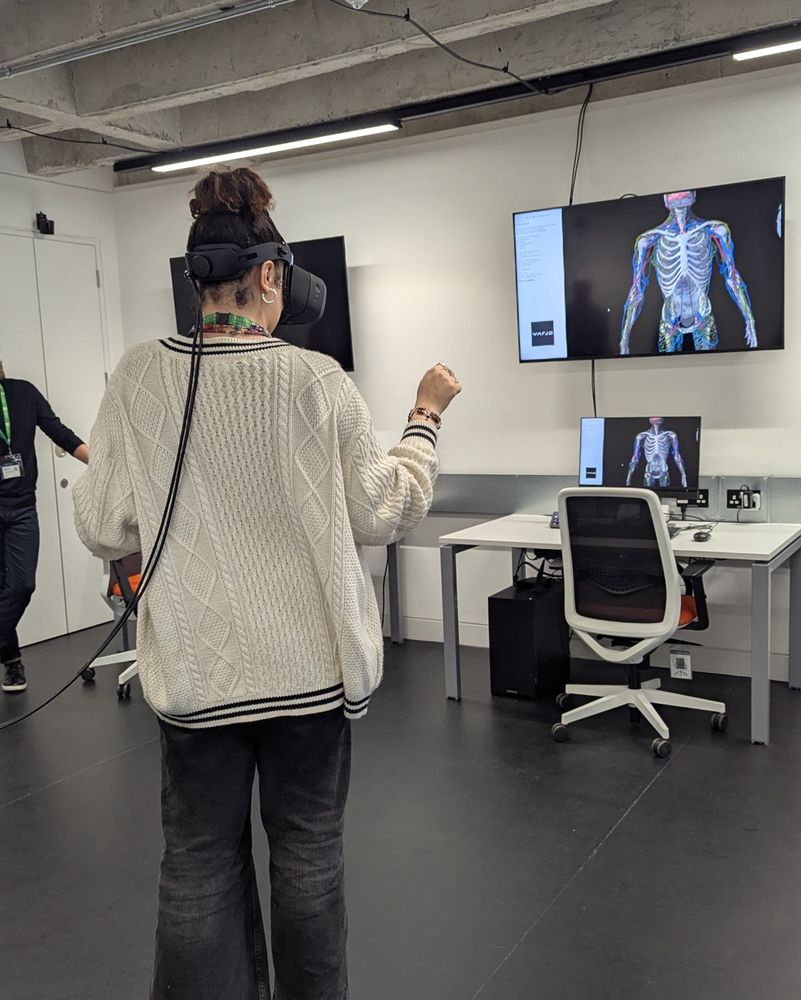 Person wearing a tethered augmented reality headset, stood in front of a screen displaying a skeleton.