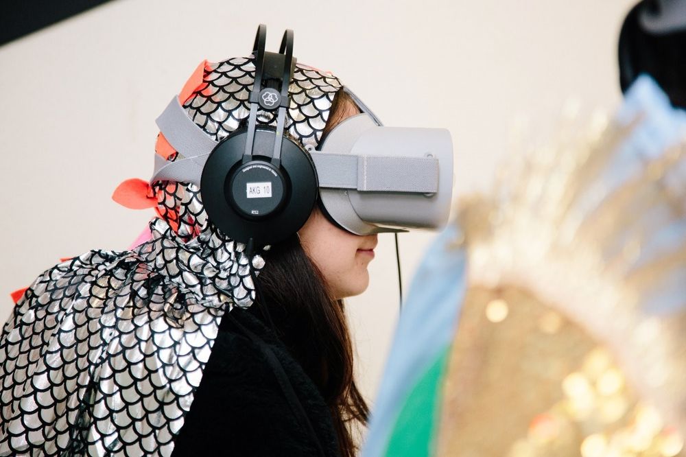 Person wearing a virtual reality headset and a shiny costume with fish-scale patterns.