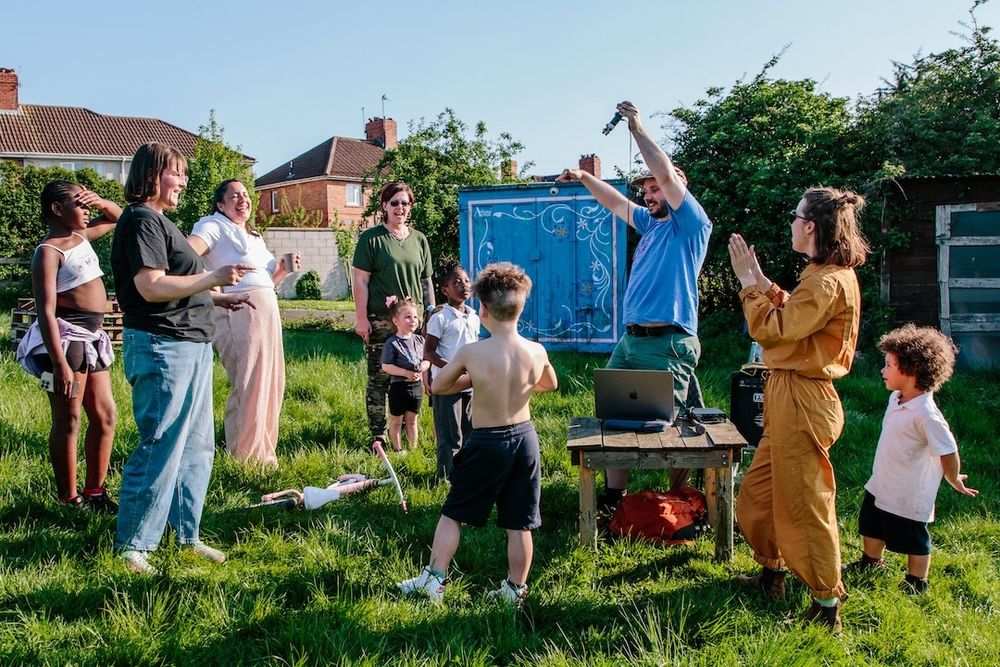 Group of adults and children celebrating around a microphone setup in an allotment.