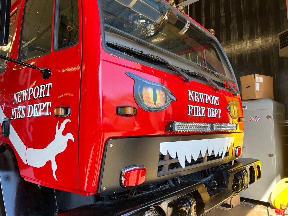 A modern off road forest fighting fire engine. Called the “monster” it has white claws painted on the door beneath the Newport Fire Dept. stencil. The front has two yellow and orange animal eye stencils. Bellow that on the grill is a white teeth cut out applied to the grill. Photo by Robert Emond. 