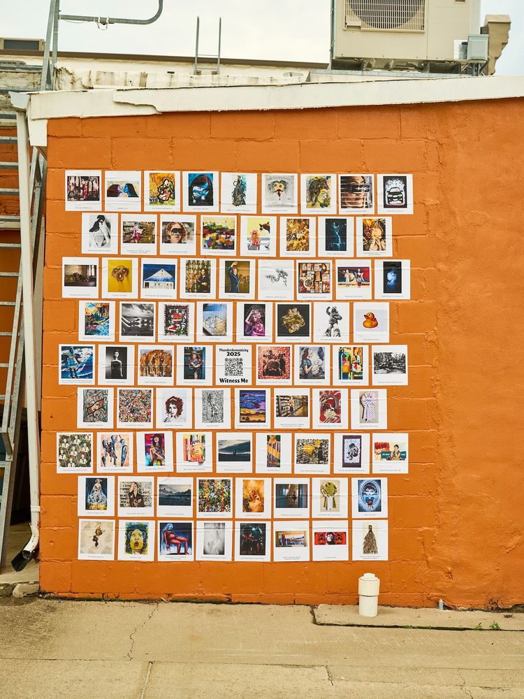 A photograph of 75 archival pigment prints of paintings, photos, drawings, prints, fiber art, and mixed media artwork glued to a bright orange exterior wall.