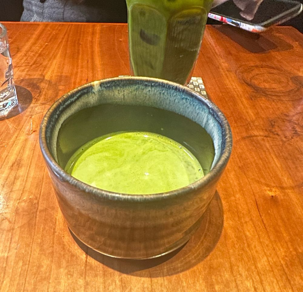 a large ceramic cup of a hot matcha drink in front of a glass of iced matcha