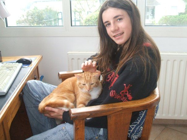 moi jeune avec les cheveux long et une bouille mimi et appareil dentaire, j'suis assise sur ma chaise et je caresse mon gros chat roux, kanel 