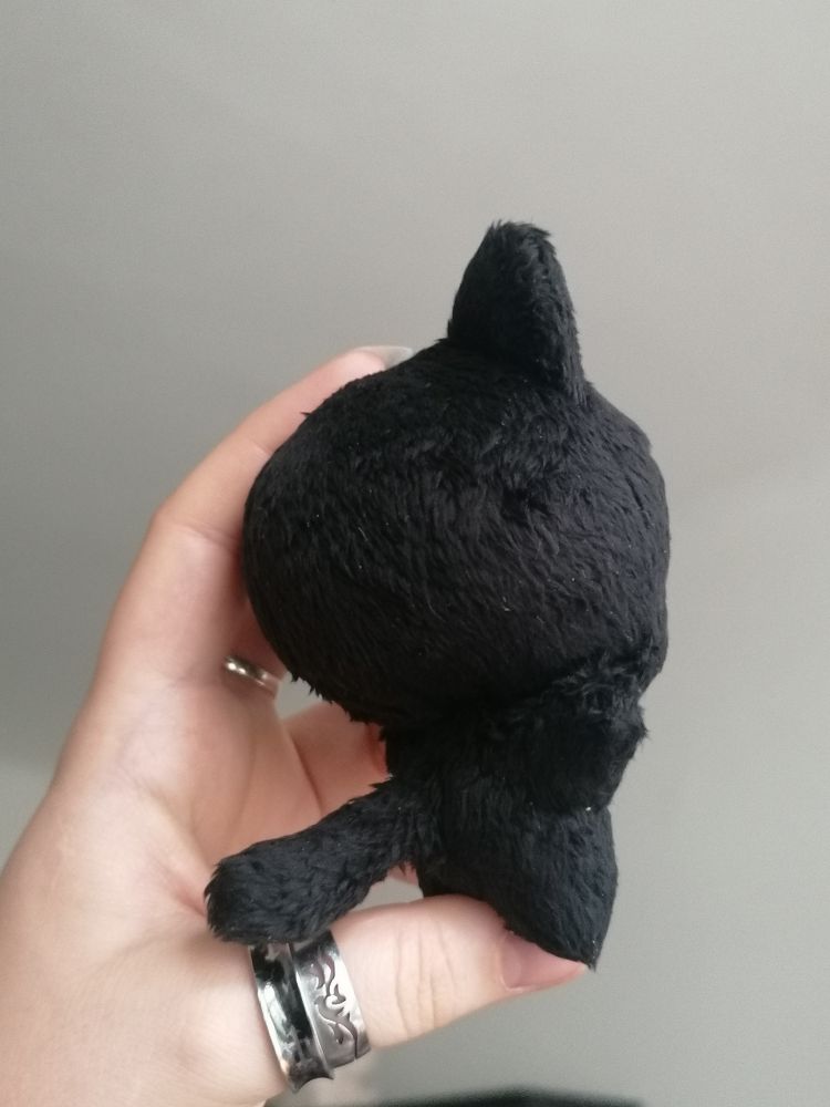 a small "chibi" plush doll of a black cat, held up in a hand, side view, showing its tail