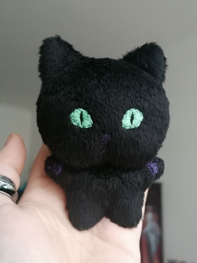 a small "chibi" plush doll of a black cat, held up in a hand, front view