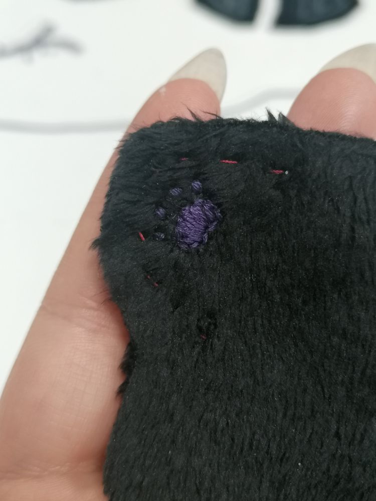 a detail of a small dark purple pawprint embroidery on a fluffy black fabric