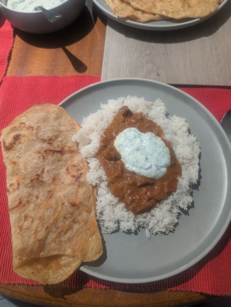 Naan bread, rice, beef curry and mint yoghurt on a grey plate
