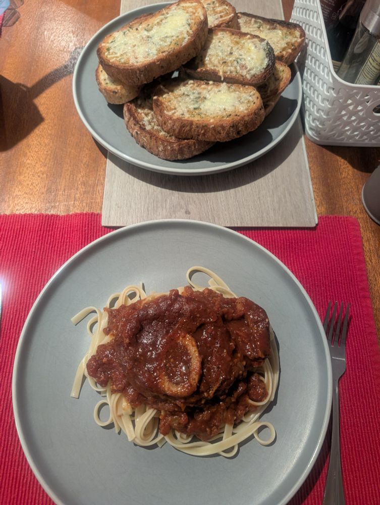 Osso bucco on fettuccini on a grey plate. Grilled sourdough with melted parmesan cheese on a grey plate