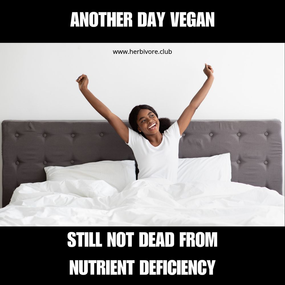 The image features a cheerful woman sitting up in bed with her arms stretched upward in a victory or stretch pose. She is smiling broadly, looking happy and healthy. The bed has white linens, and the headboard is gray and tufted. At the top of the image, text reads "ANOTHER DAY VEGAN" in bold capital letters, and at the bottom, it states "STILL NOT DEAD FROM NUTRIENT DEFICIENCY" in smaller capital letters. A website link "www.herbivore.club" is also present at the top. The image seems to be a lighthearted dispelling of the myth that plantbased diets are inherently nutrient-deficient.